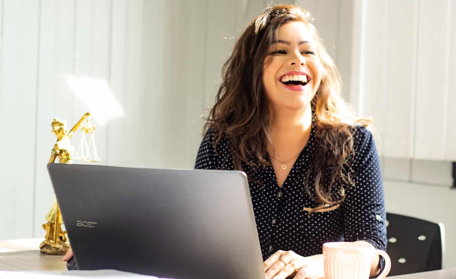 woman sitting at laptop laughing thanks for freedom of starting her own online subscription business